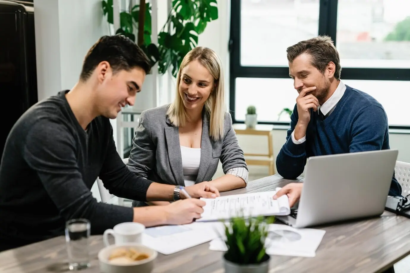 A young, happy couple signing an agreement with a real estate agent during an office meeting.
