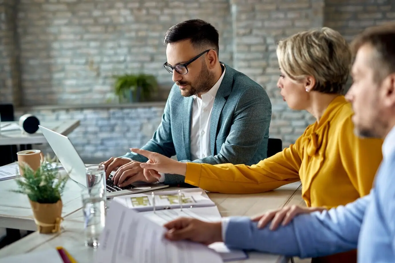 A financial advisor working on a computer while meeting with a couple in the office.