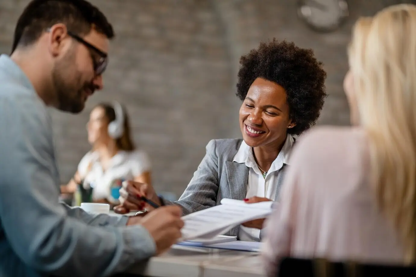 A smiling African American insurance agent reviews the contract terms with a couple and points to where they need to sign in the office.